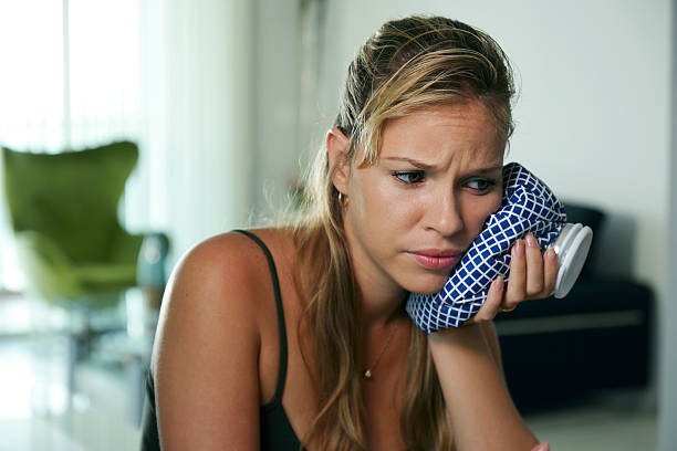a woman using a compress to ease her tooth pain