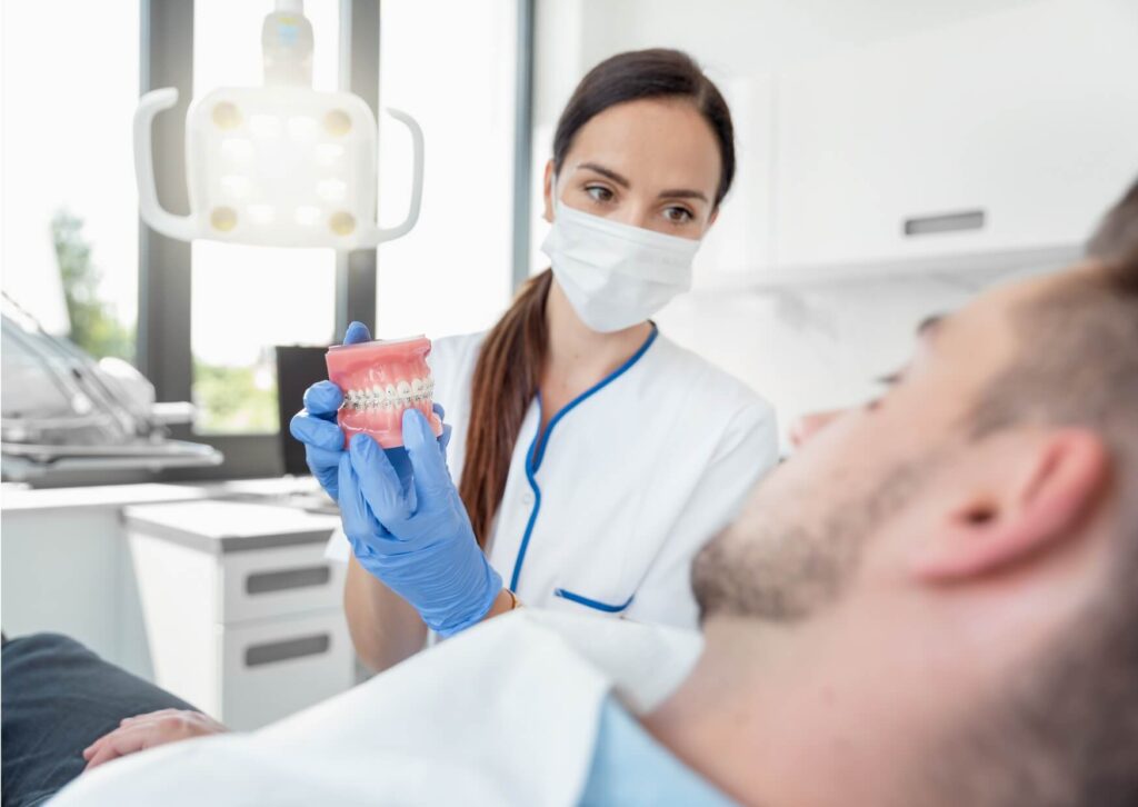 Dentist using a jaw model to explain TMJ and TMD causes, symptoms, and treatment options during a patient consultation.