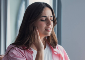 Woman holding her jaw in discomfort, illustrating common TMJ and TMD symptoms such as jaw pain and tenderness.