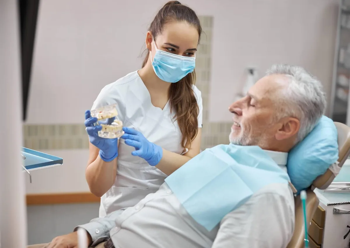 Dentist discussing affordable dental implant options with an older patient using a dental model.